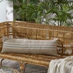 Wicker outdoor sofa with a striped pillow and plants in the background