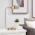 A table lamp with a brass finish, featuring a sleek, modern design with a rounded shade and a flat base.