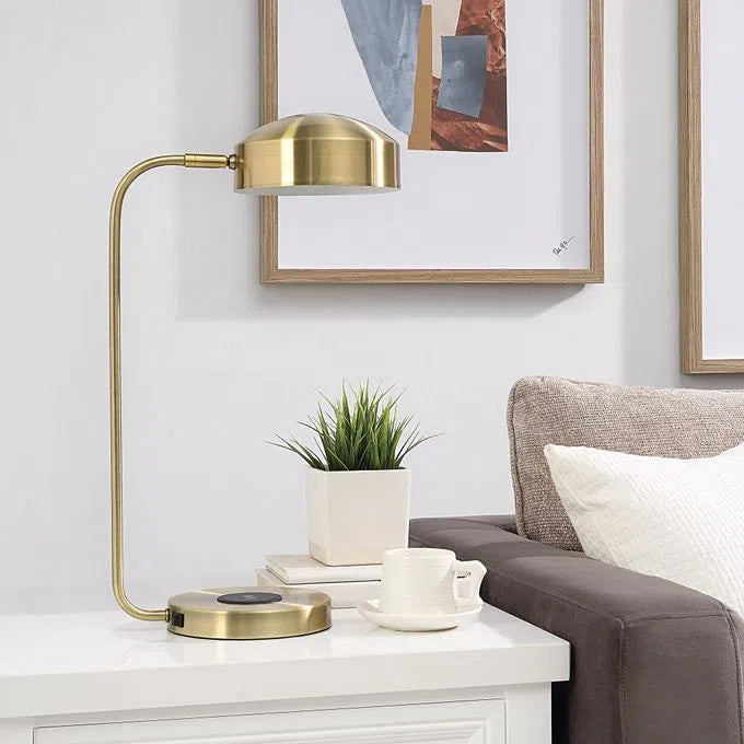 A table lamp with a brass finish, featuring a sleek, modern design with a rounded shade and a flat base.
