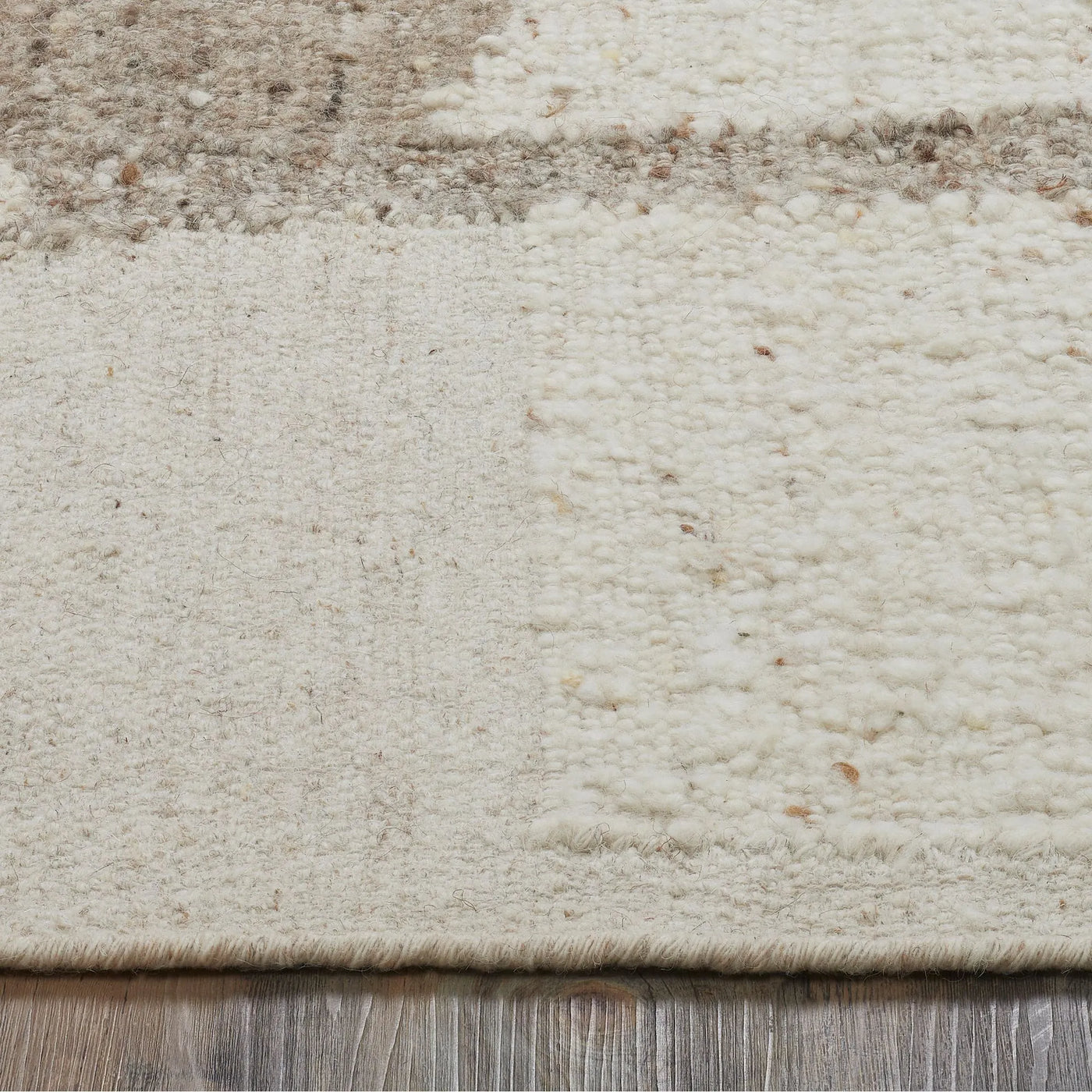 Close-up of a textured beige rug with subtle patterns on a wooden floor.