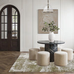 Modern interior with a round black marble table, white vase with greenery, and beige ottomans on a patterned rug.