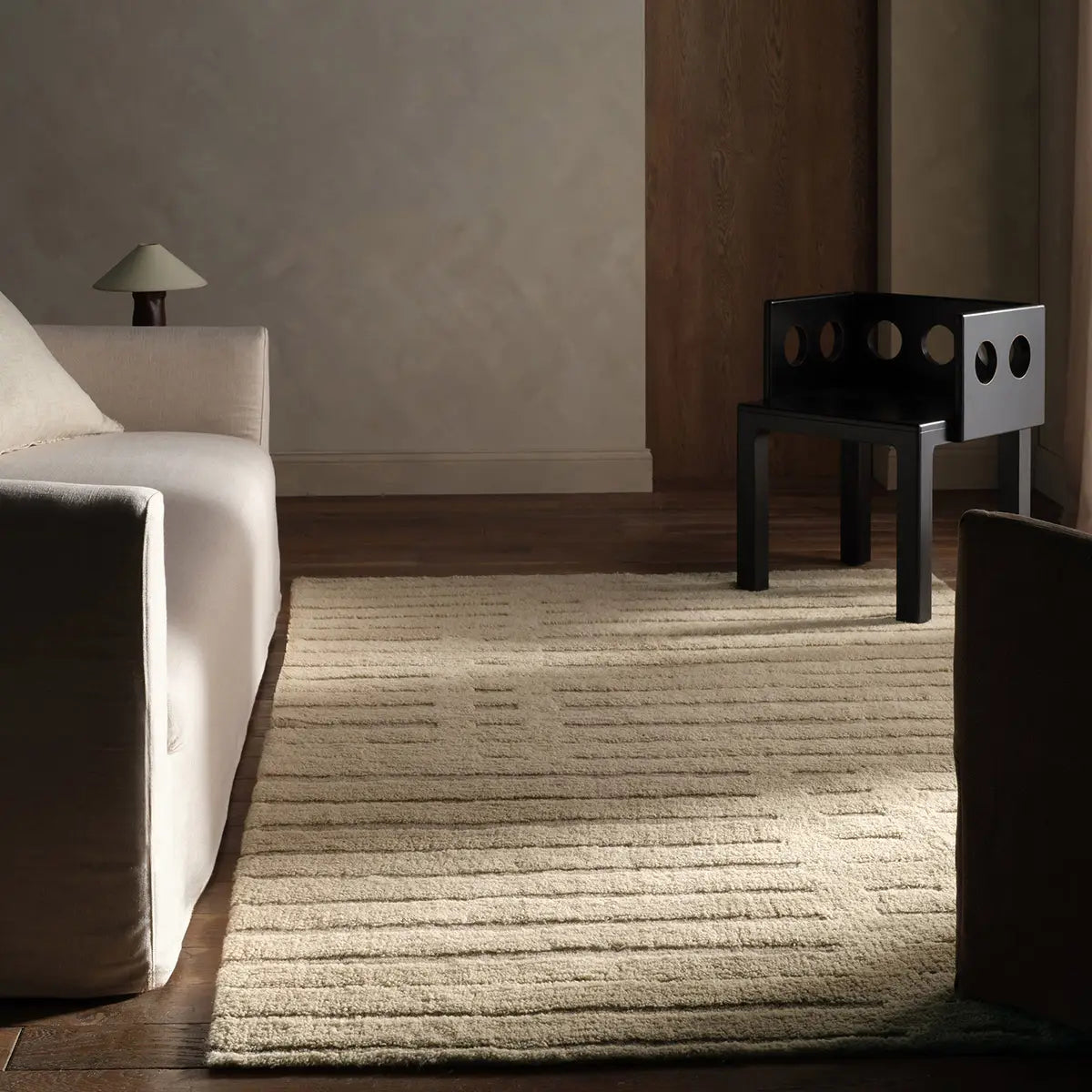 Modern room interior with a textured rug, white sofa, and black chair.