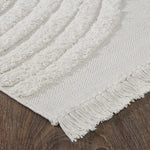 An off-white, hand woven cotton area rug with a geometric pattern and fringe edge.