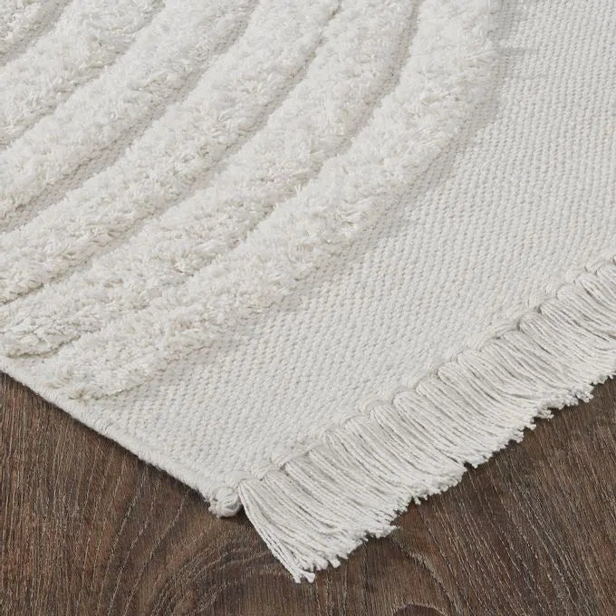 An off-white, hand woven cotton area rug with a geometric pattern and fringe edge.