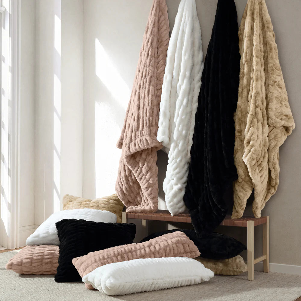 Knitted blankets and pillows in various colors on a wooden bench against a neutral wall.