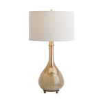 A table lamp with a tapered drum shade in off-white linen, a polished gold-finished stem, and a pear-shaped base in a warm champagne-gold tone with subtle distressed blue-green patina details near the bottom, set against a plain white background.