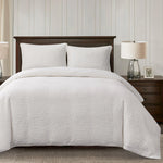 White quilted comforter set on a bed with wooden headboard and nightstands.