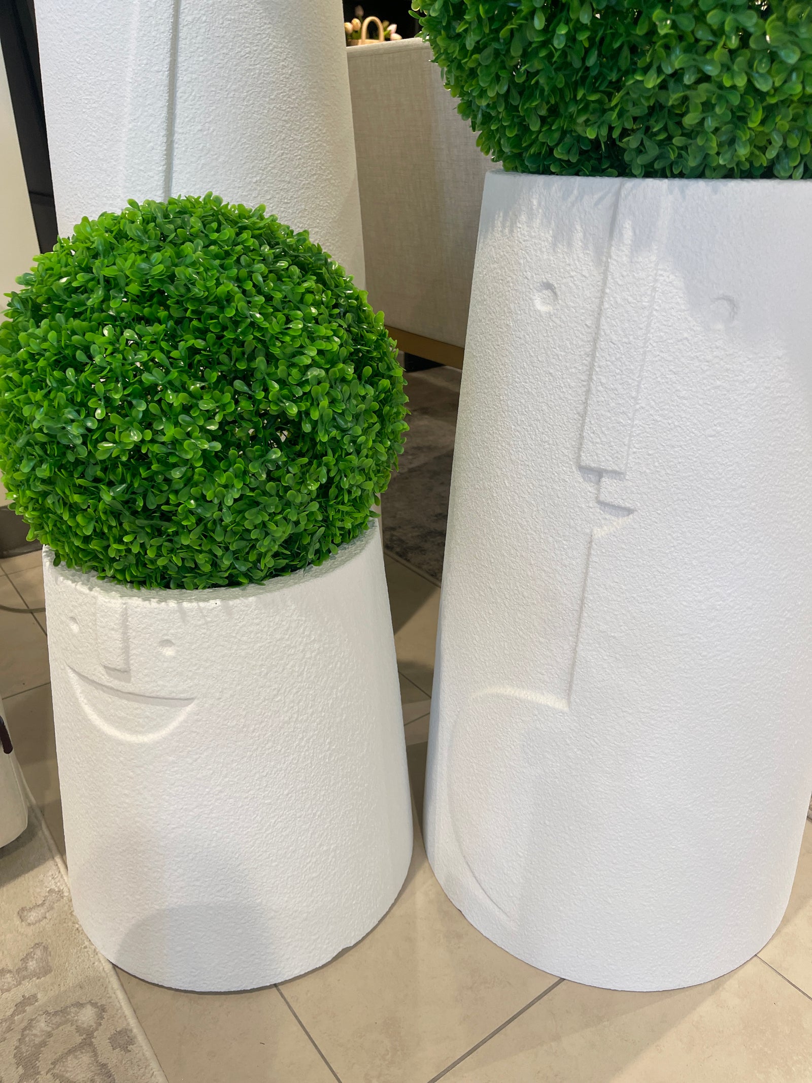 Two white, textured, rounded planters of different sizes, each containing a spherical artificial green plant.