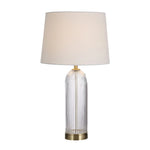 Table lamp with clear cylindrical glass base and beige fabric shade on a white background