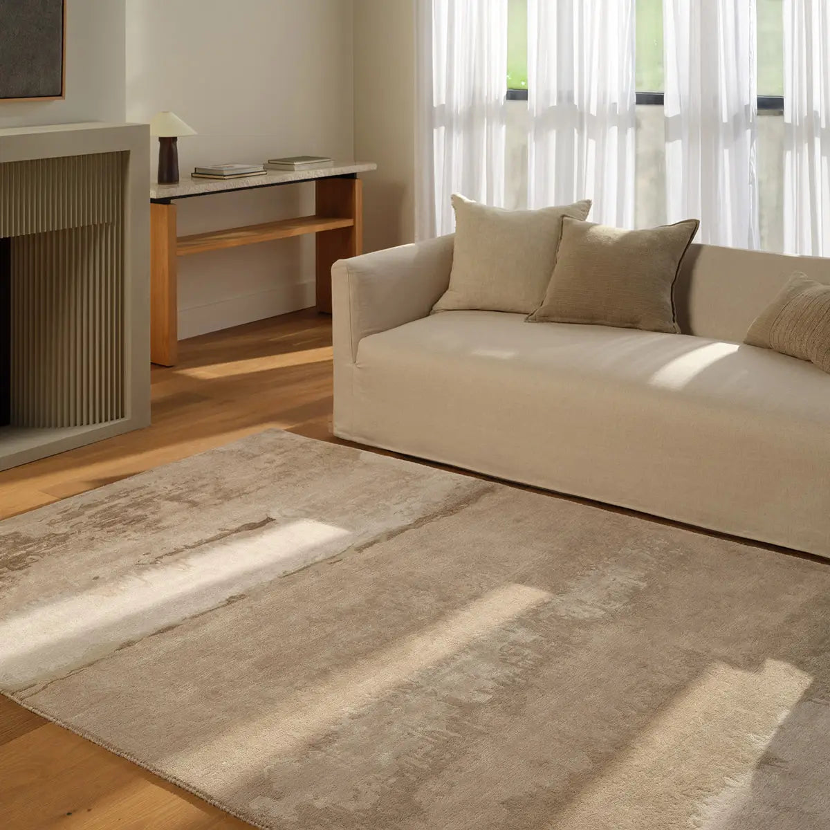 Beige sofa with decorative pillows in a living room setting with a large rug.