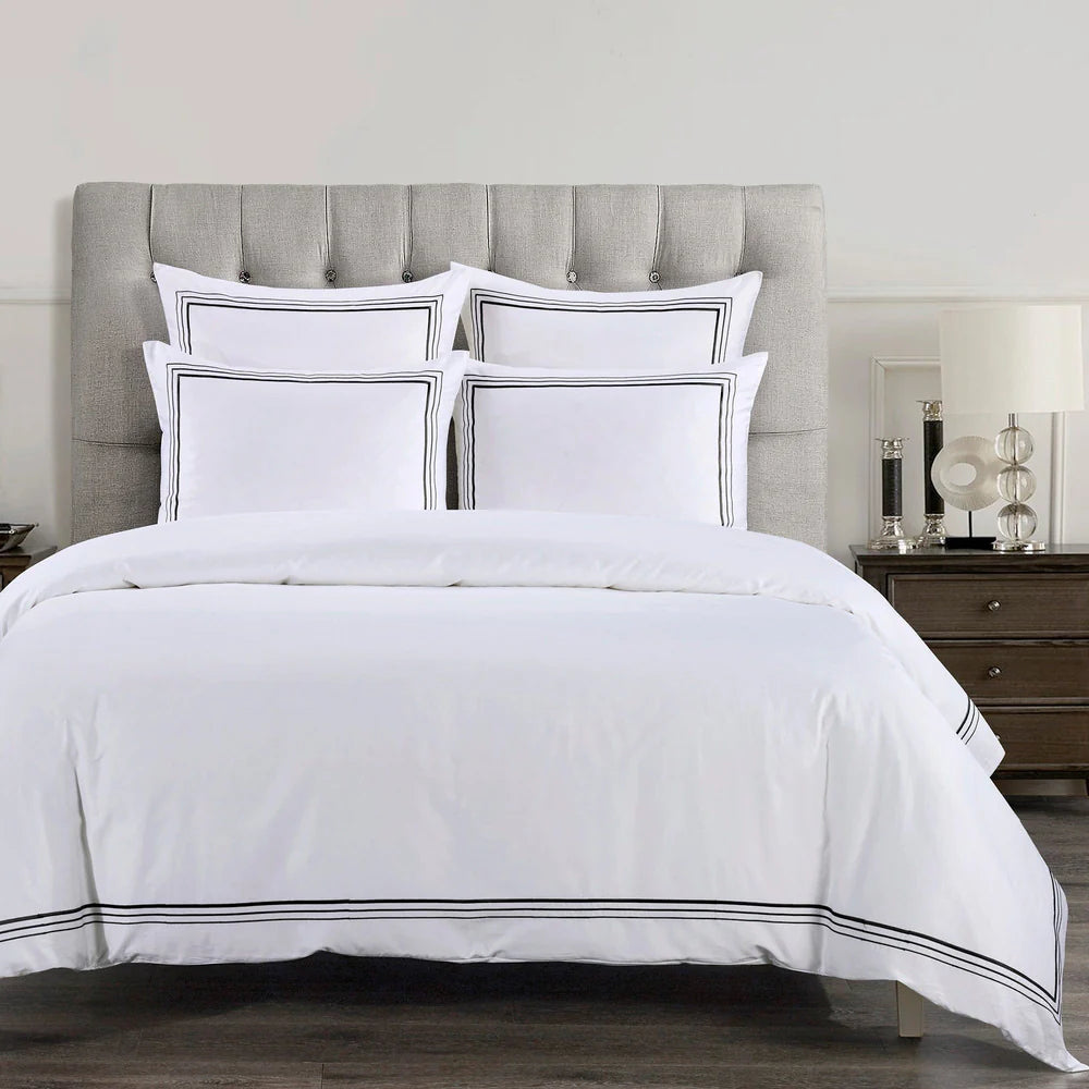 White bedding set with black trim on a bed with a gray upholstered headboard.