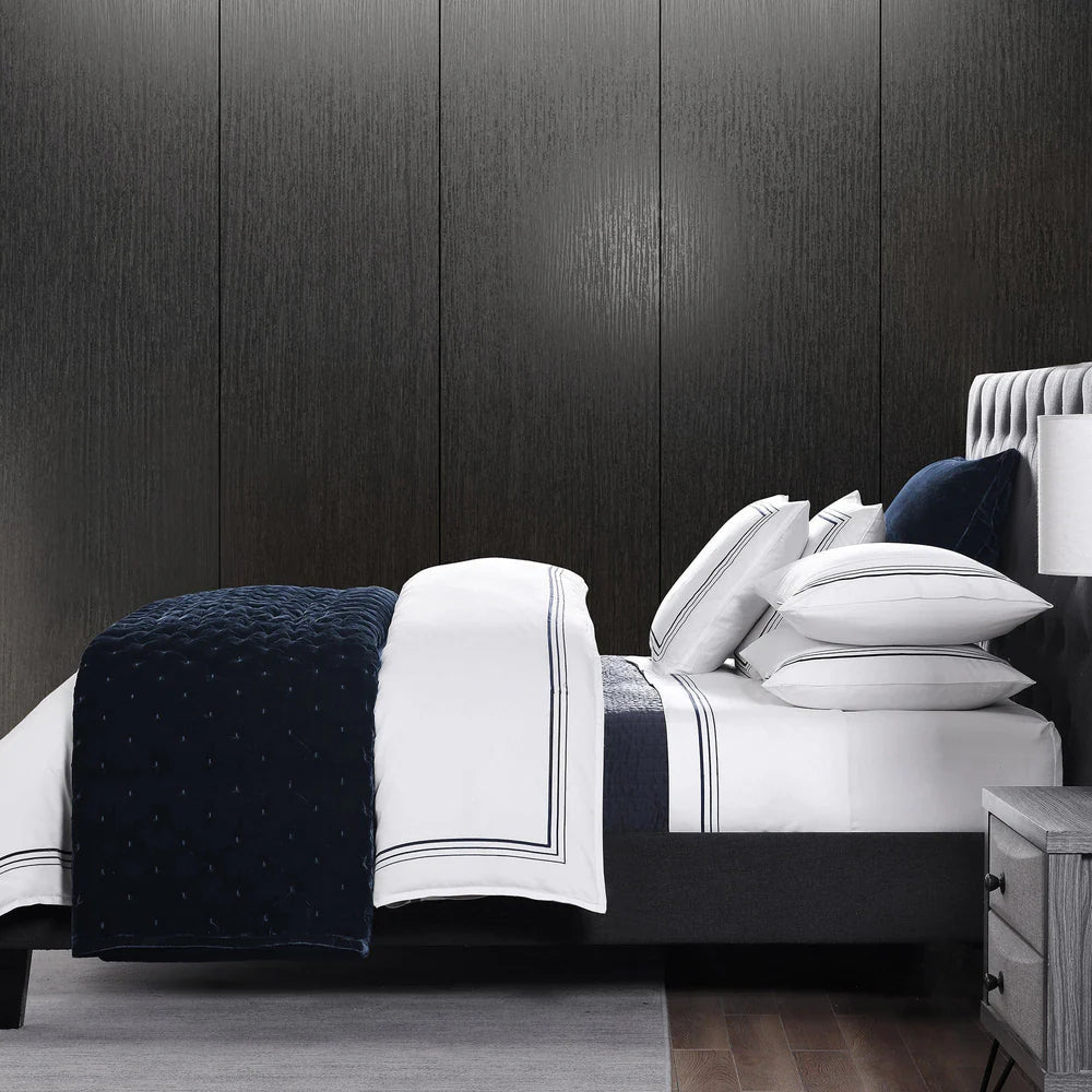 Bed with navy and white bedding against a dark paneled wall.