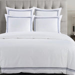 White bedding set with blue trim on a bed with a gray upholstered headboard.