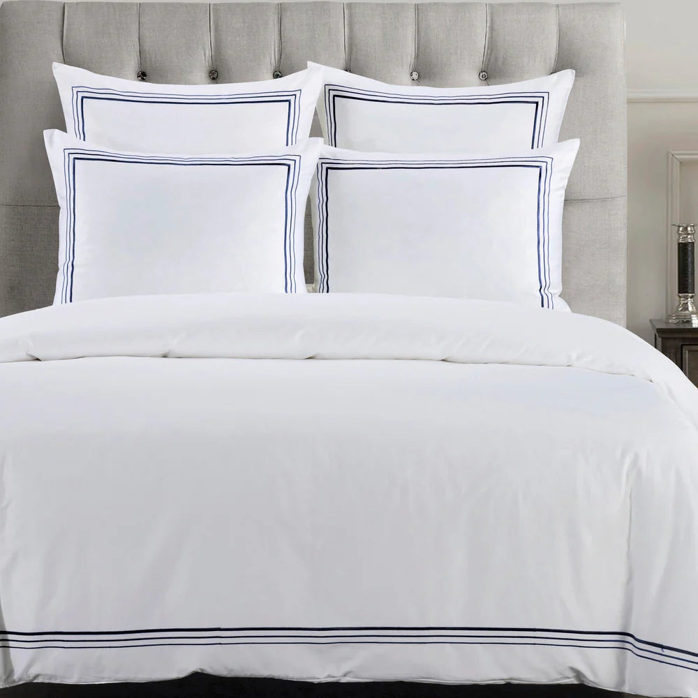 White bedding set with blue trim on a bed with a gray upholstered headboard.