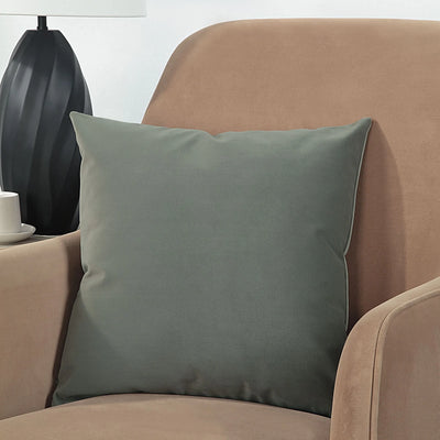 Gray pillow on a brown armchair with a black lamp and white wall in the background