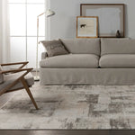 A white area rug with a geometric pattern featuring various shades of grey and a subtle wood floor appearance.