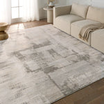 A white area rug with a geometric pattern featuring various shades of grey and a subtle wood floor appearance.