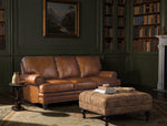 Brown leather sofa and ottoman in a room with bookshelves and a painting on the wall.