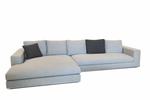 Gray sectional sofa with two dark cushions on a white background