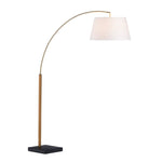 A brass floor lamp with a white lampshade, having a curved stand supported by a black base.