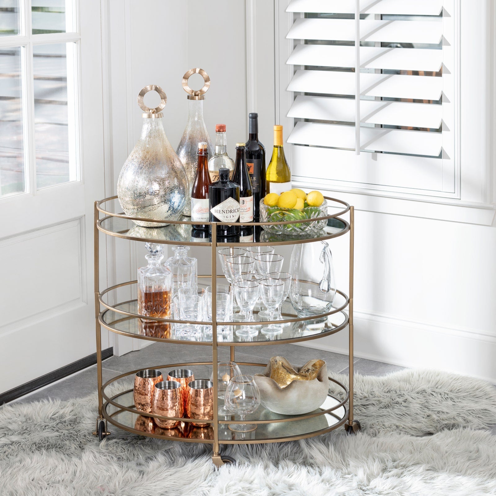 Three-tiered gold bar cart with drinks and glasses in a home setting
