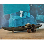 Decorative metal bowl with spherical objects on a wooden surface in front of a blue abstract painting.