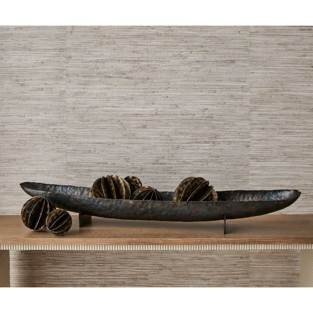 Decorative metal bowl with spherical elements on a wooden surface against a textured wall.