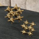 Two gold metallic sculptures on a dark surface