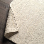 Close-up of a textured beige rug corner on a wooden floor