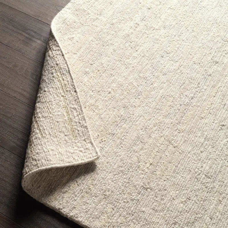 Close-up of a textured beige rug corner on a wooden floor