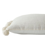 A square-shaped decorative pillow with solid pattern and pom pom detailing on the edges, primarily in a natural white color.