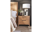 Wooden nightstand with lamp next to a bed in a bedroom setting