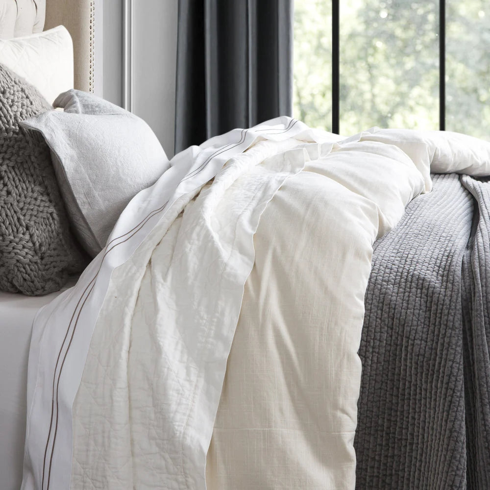 Neatly made bed with white bedding and gray pillows in a bedroom setting.