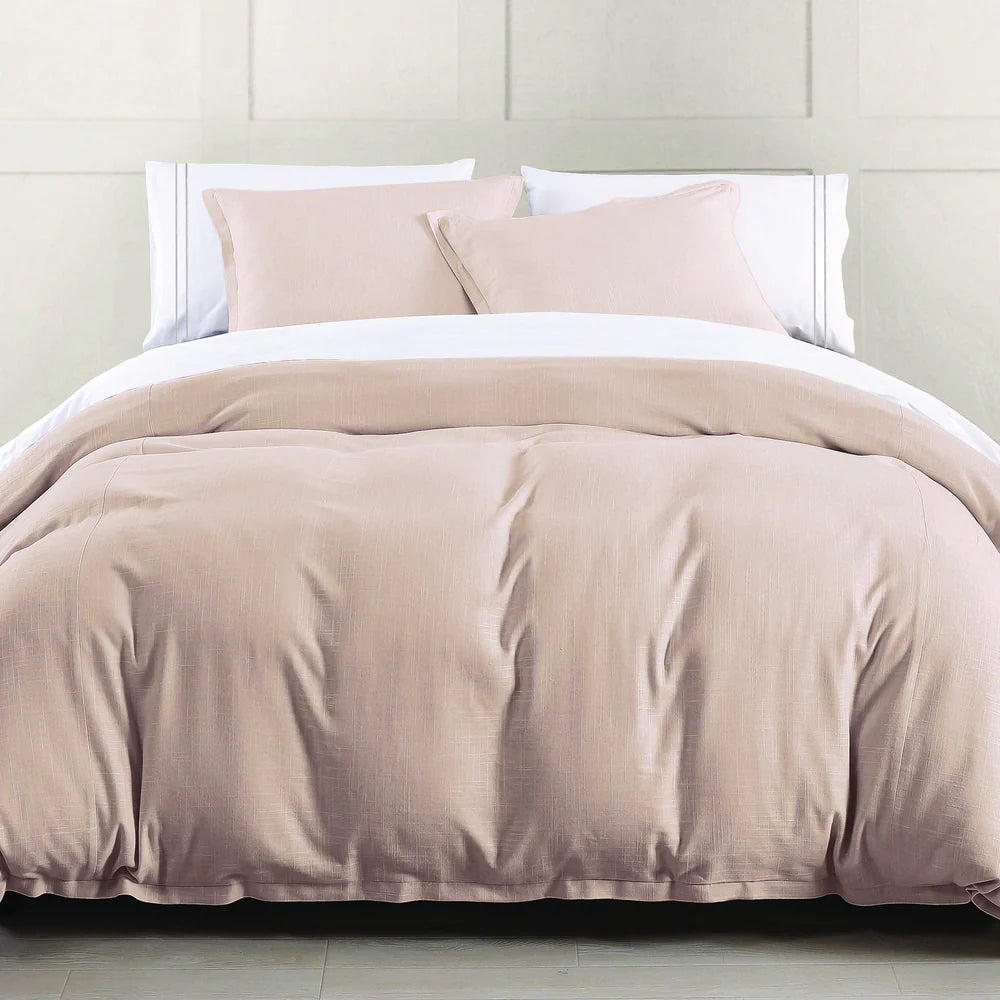 Beige comforter set on a bed with white pillows against a light-colored wall.
