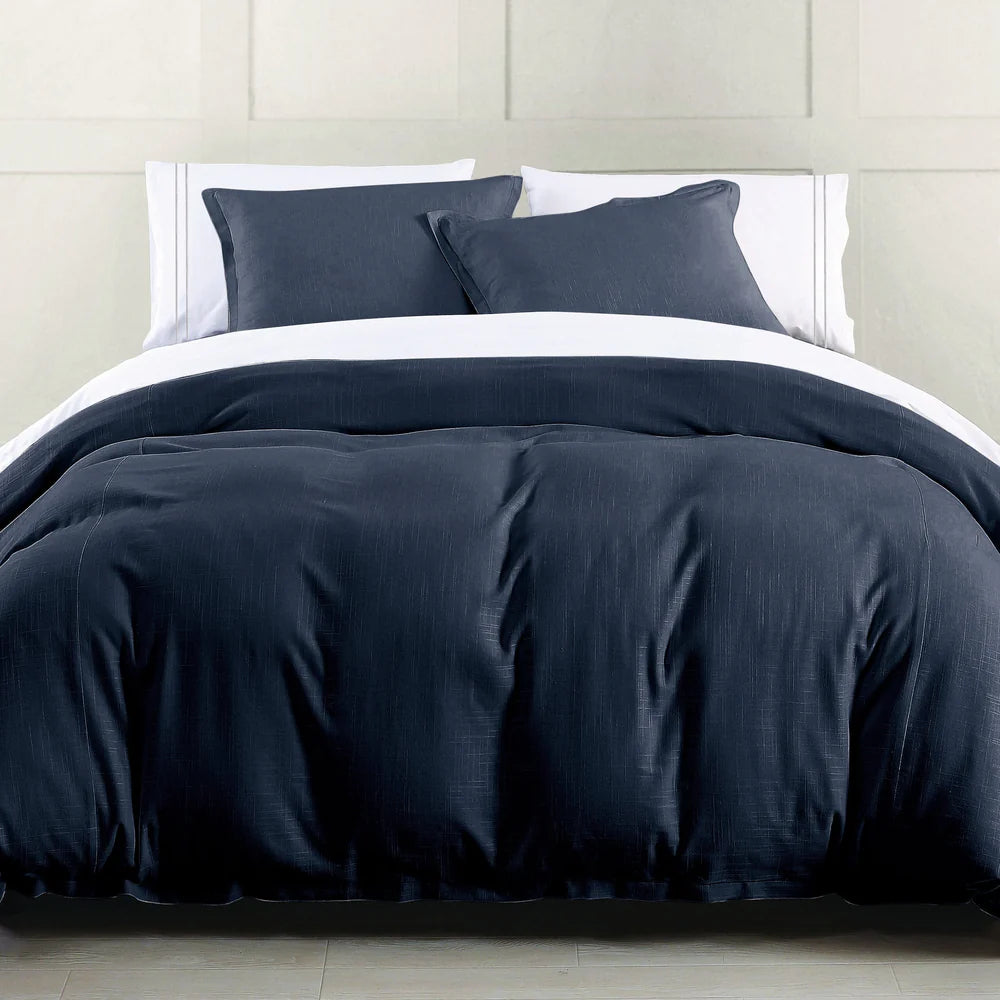 Dark blue bedding set on a bed with white pillows against a neutral wall.