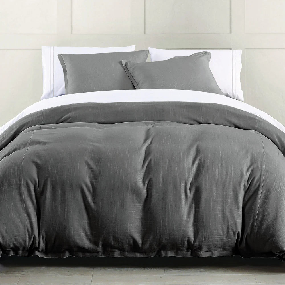 Gray bedding set on a bed with white pillows against a neutral wall.