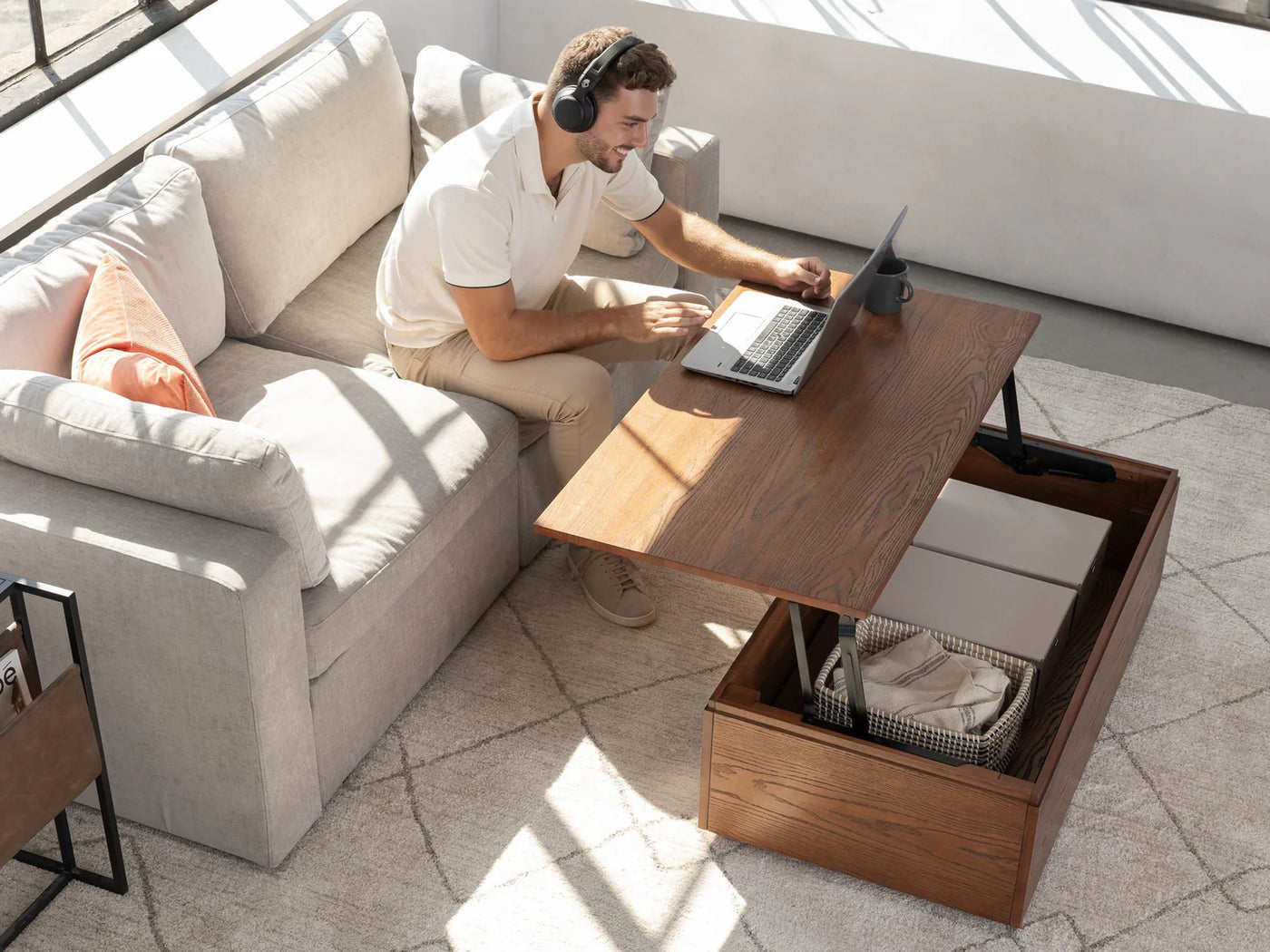 Man using a laptop on a wooden coffee table with storage compartments in a modern living room.
