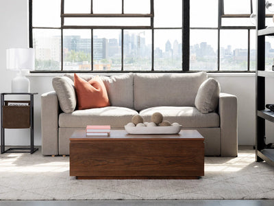 Modern living room with a beige sofa, wooden coffee table, and large windows with a cityscape view.