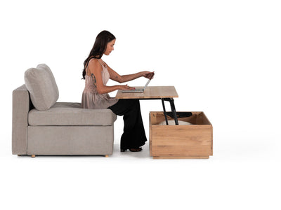 Woman using a laptop on a convertible sofa with a wooden side table.