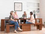 Four women sitting around a wooden dining table in a modern kitchen.