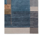 A modern geometric patterned area rug featuring shades of blue, gray, and beige.