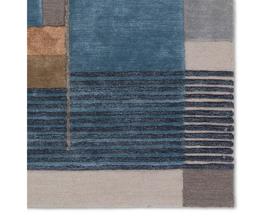 A modern geometric patterned area rug featuring shades of blue, gray, and beige.