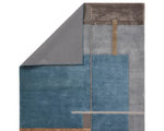 A modern geometric patterned area rug featuring shades of blue, gray, and beige.