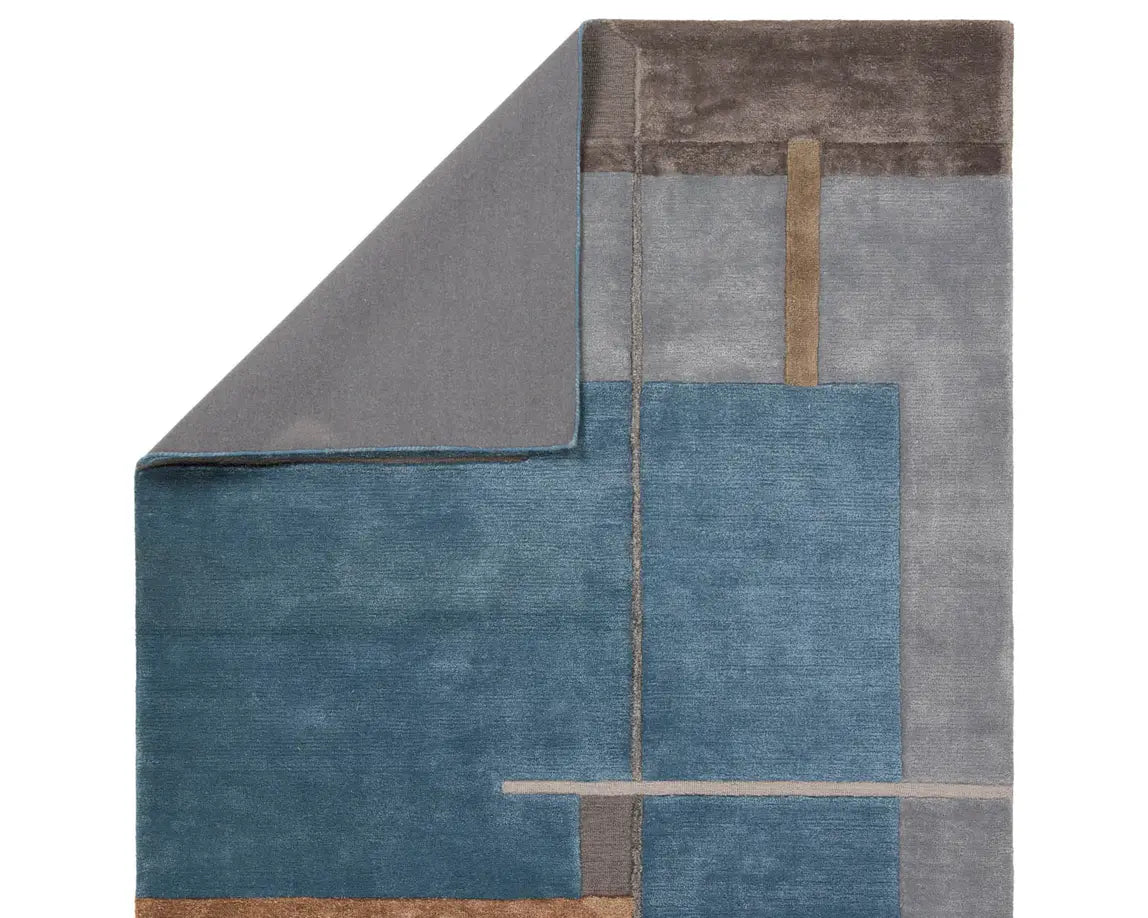 A modern geometric patterned area rug featuring shades of blue, gray, and beige.