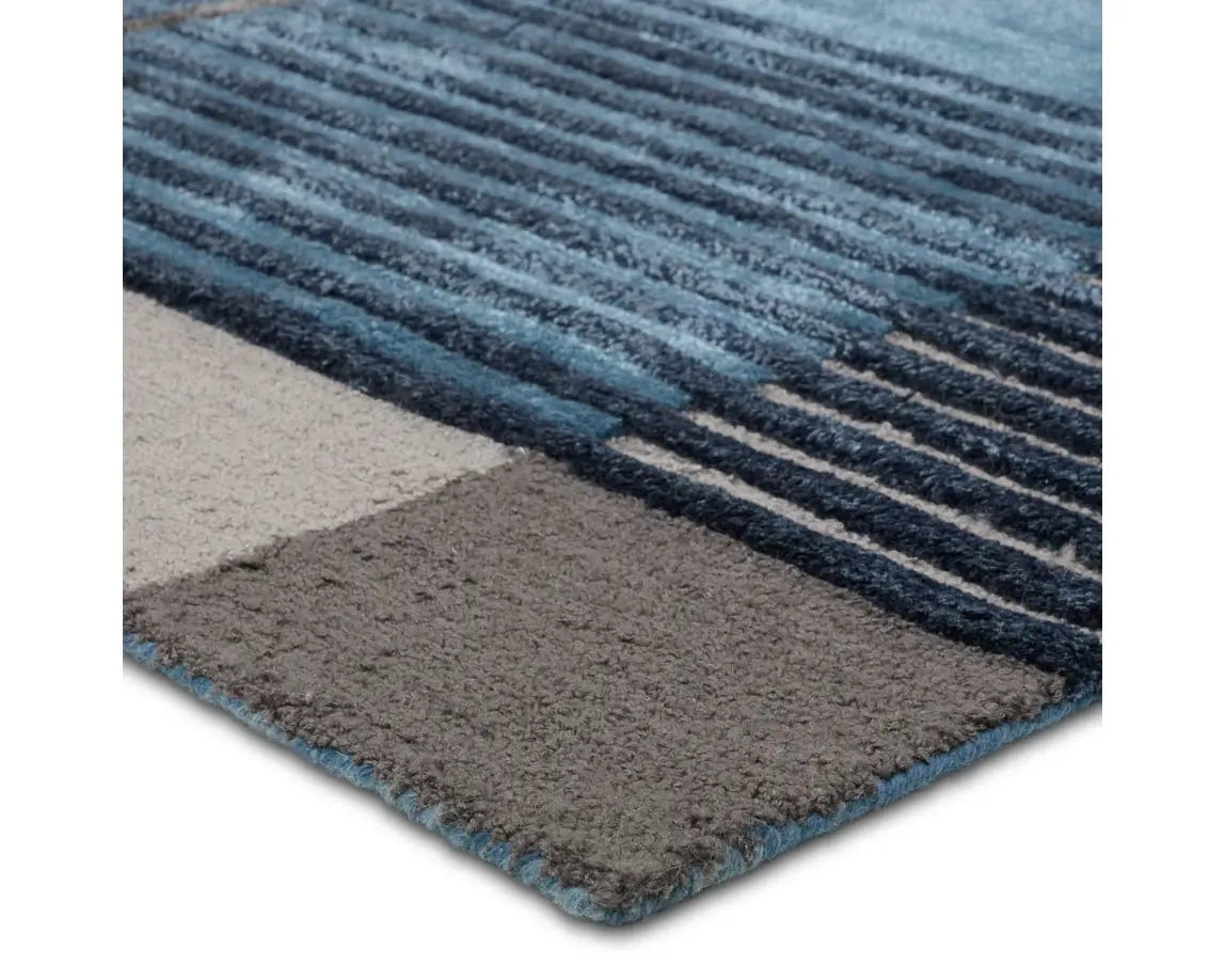 A modern geometric patterned area rug featuring shades of blue, gray, and beige.