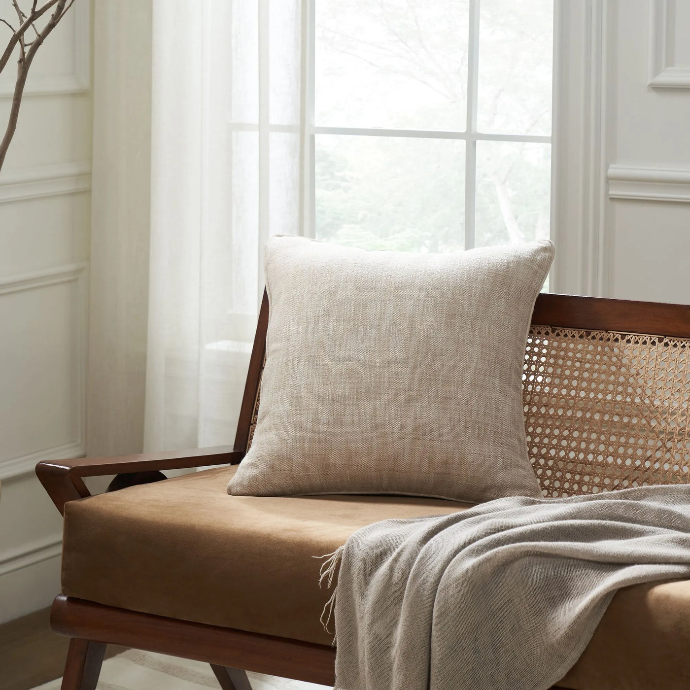 Wooden chair with a beige cushion and blanket in a bright room.