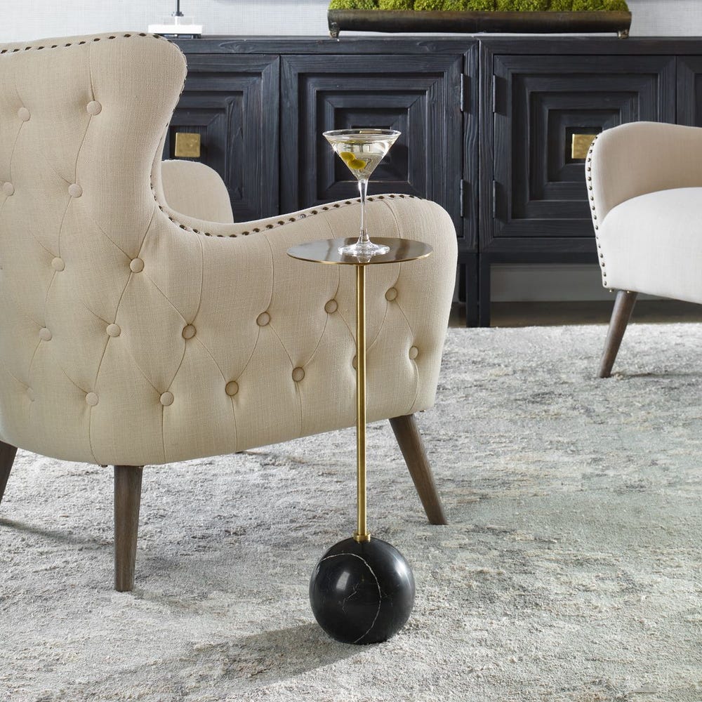 Decorative side table with a glass of champagne next to a tufted armchair in a stylish room.
