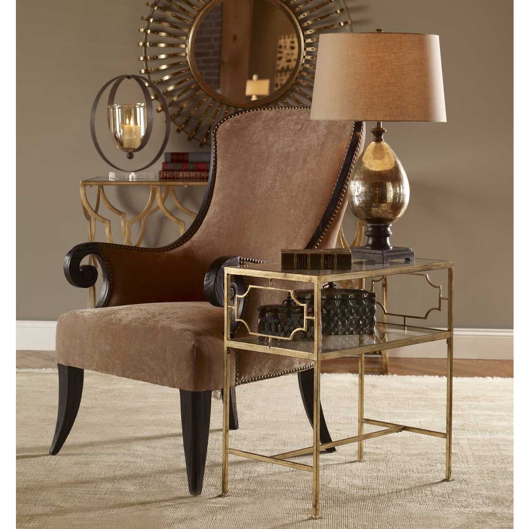 Decorative interior scene with a brown armchair, gold table, and lamp against a beige wall.
