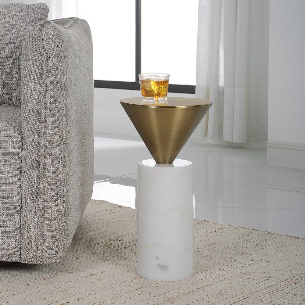 Modern side table with gold cone top and marble base next to a gray sofa in a living room.