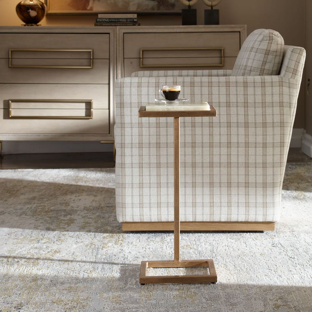 Small wooden side table with a glass of coffee in front of a plaid armchair.